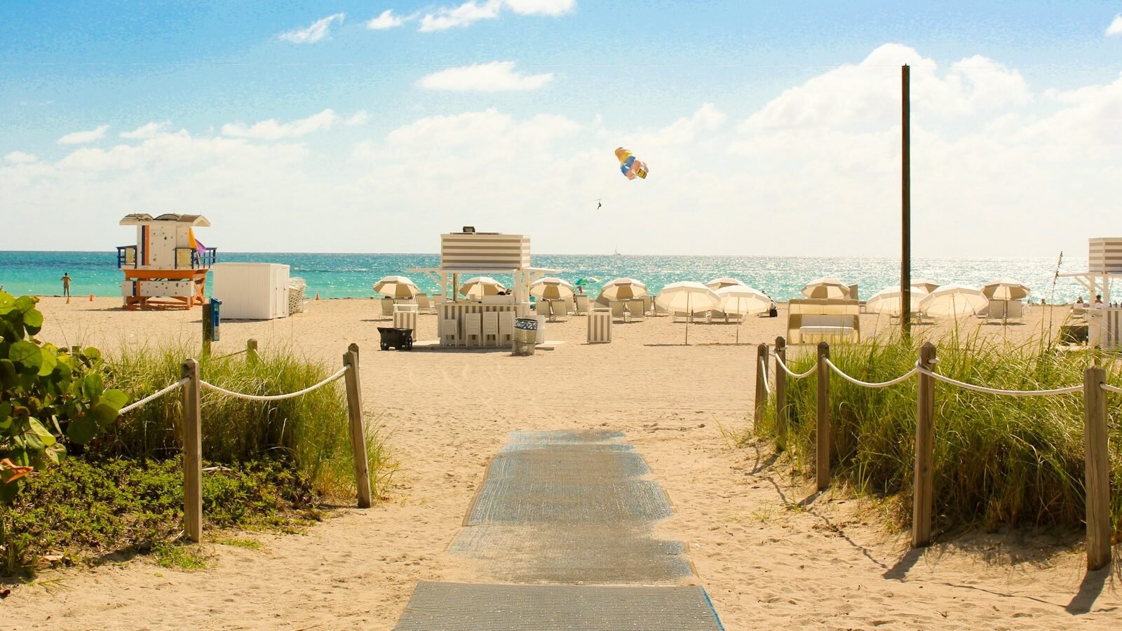 gray pathway leading to parasol, lifeguard house, and sea a daytime